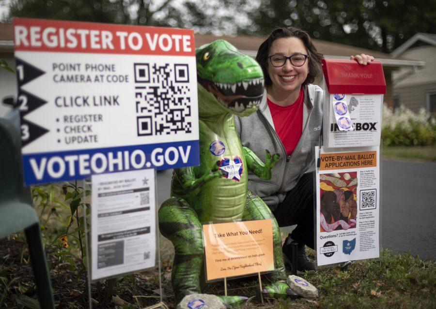 Tiffany Rumbalski sits beside the voting materials, including absentee ballot requests, that shes providing outside her home in Hilliard, Ohio on Tuesday, Sept. 1, 2020. The inflatable tyrannosaurus rex, Vinny Voter, helps draw attention to the display and encourage passers by to take the free materials and get a selfie. (Adam Cairns/The Columbus Dispatch/TNS)