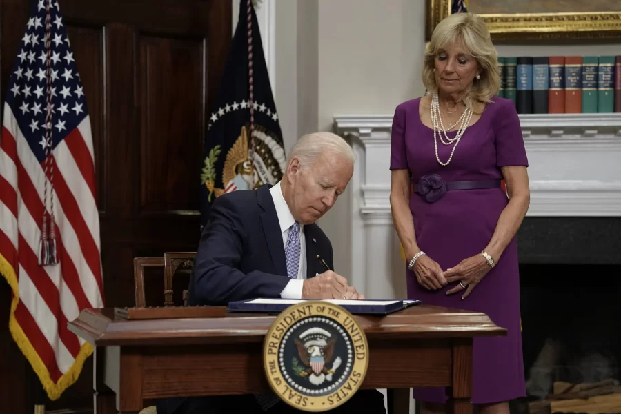 Joe Biden, sitting in the Oval Office, signs a bipartisan gun reform package.
