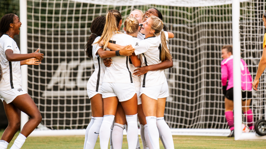 The women's soccer team celebrates in front of the net.