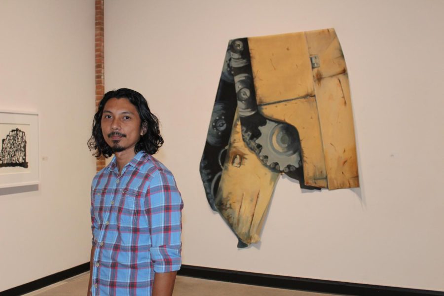 A photograph of a man standing next to a piece of art