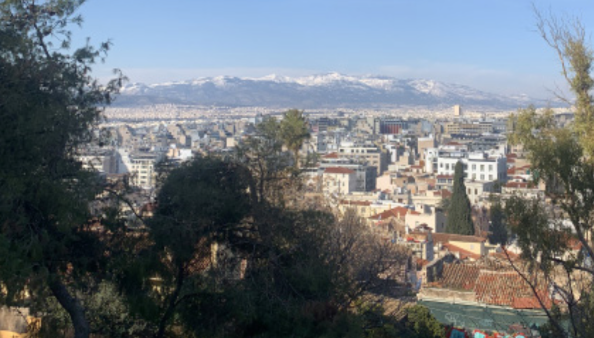 A view of the densely-packed buildings that comprise the city of Athens, Greece, nestled between mountain ranges and containing unparalleled history and culture.