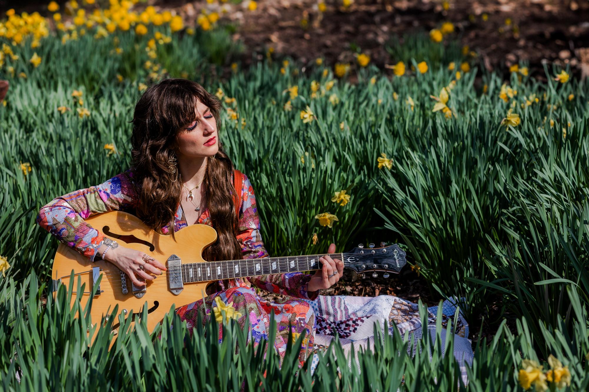 Ashley Virginia plays her guitar in a field.